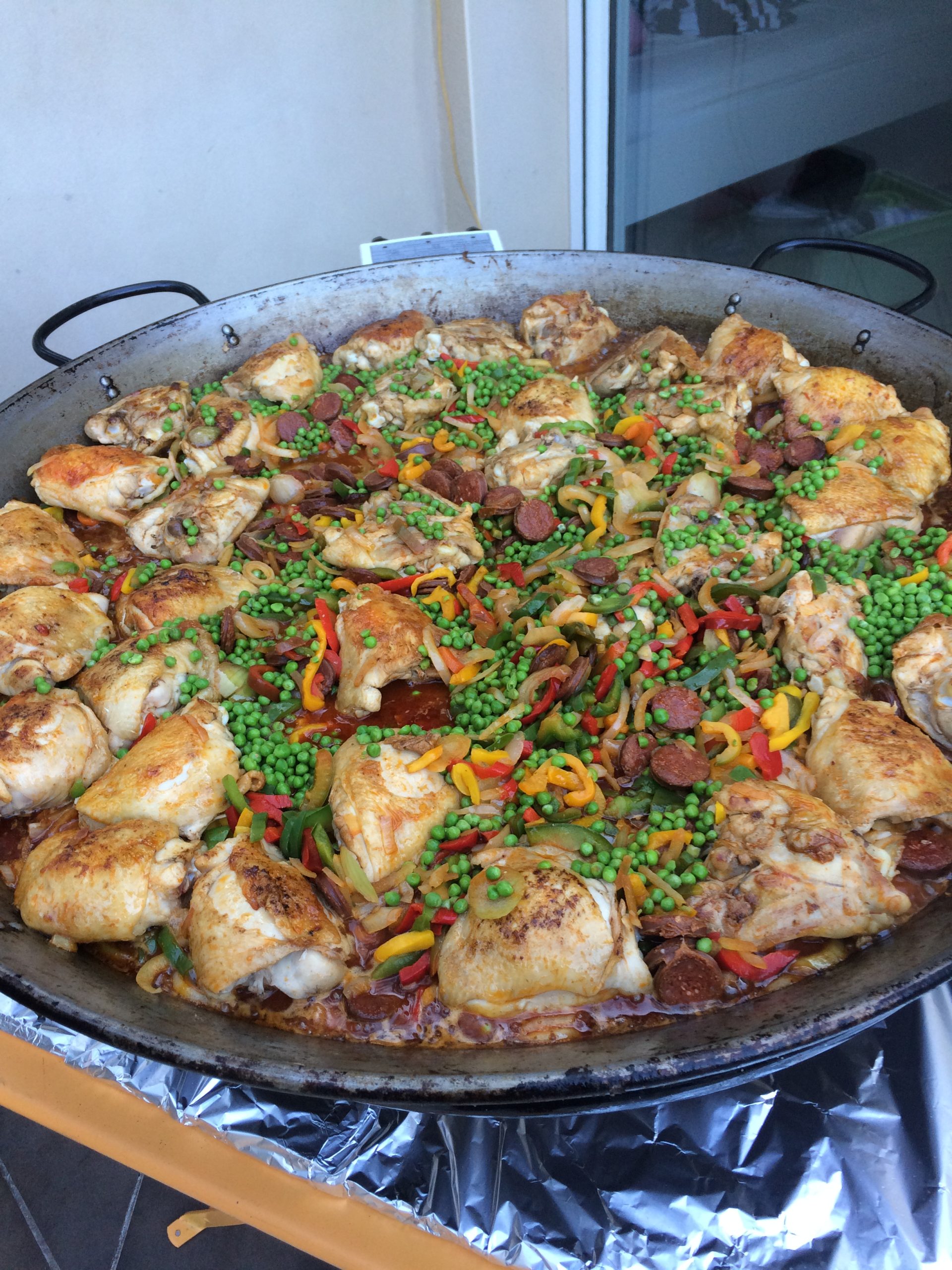 Grande poêle de paella au poulet, chorizo, poivrons et petits pois, cuite en extérieur sur un réchaud.